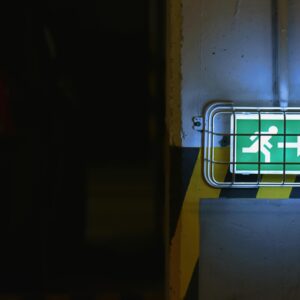 Green emergency exit sign with arrow in dimly lit area, emphasizing safety.