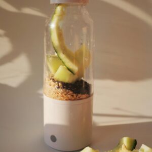 A portable blender filled with melon, seeds, and grains, perfect for a nutritious smoothie on the go.