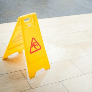 A bright yellow caution sign placed on a tile floor indicating a wet area for safety.