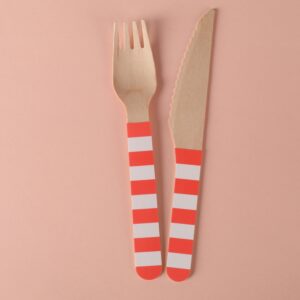 Minimalist eco-friendly wooden fork and knife on a pink background with striped handles.