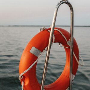 A bright orange lifebuoy hangs on a boat over still serene waters, symbolizing safety and preparation.