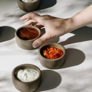 Hand reaching for ceramic bowls with sauces in sunlight, showcasing delicious variety.