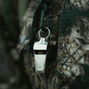 Close-up of a shiny silver whistle hanging against a camouflage-patterned fabric background.