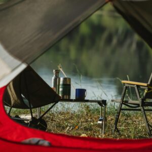 Through tent hole view of portable chairs and table with thermoses on grass shore against lake