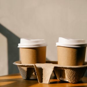 Two disposable coffee cups on a table with soft sunlight creating shadows, emphasizing eco-friendly packaging.