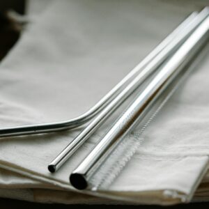Collection of stainless steel straight and bent straws placed on reusable bags on table