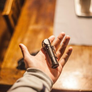 Close-up of a hand holding a flashlight on a wooden table indoors, warm lighting.