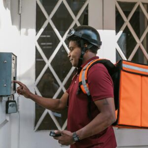 Delivery person with insulated bag pressing doorbell at entrance, providing home delivery service.