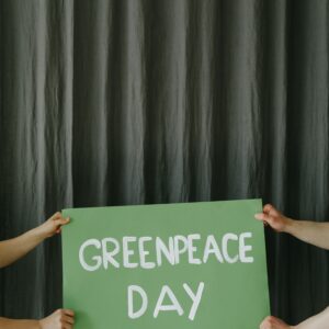 Hands holding a green Greenpeace Day sign against a dark curtain backdrop.